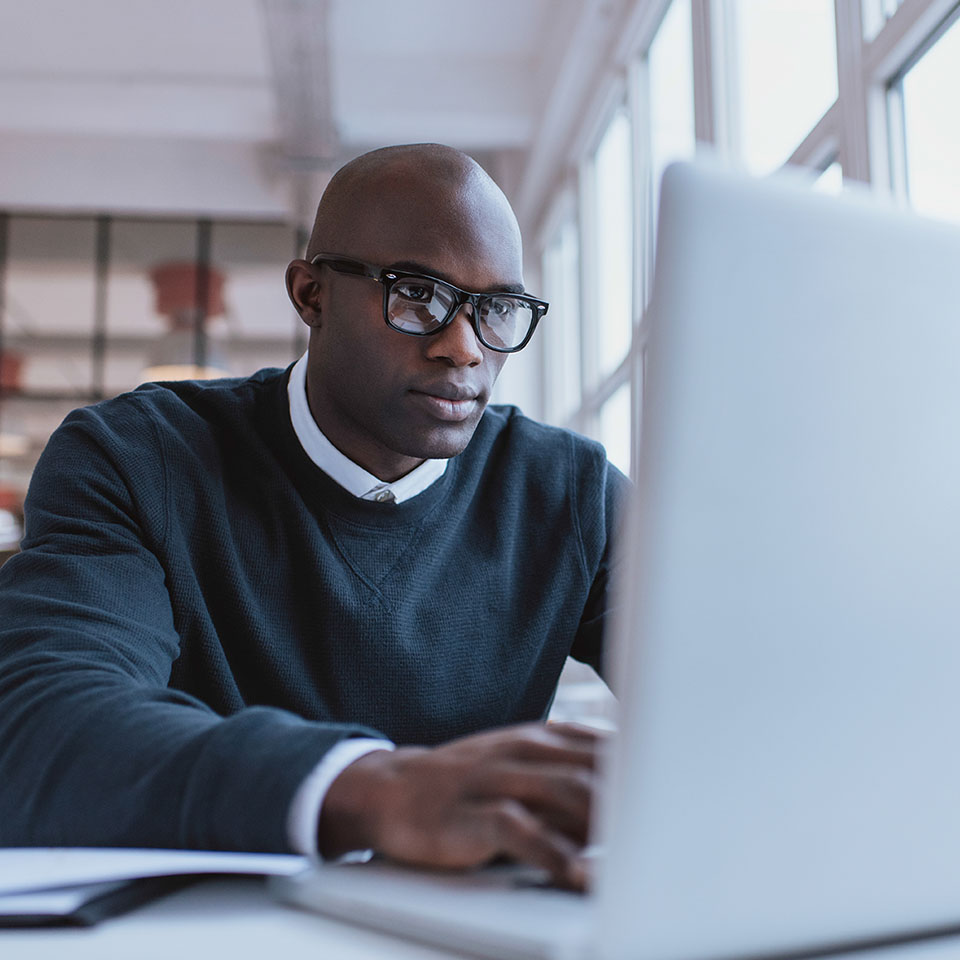 Young businessman working on his laptop in office. Young african executive sitting at his desk surfing internet on laptop computer.